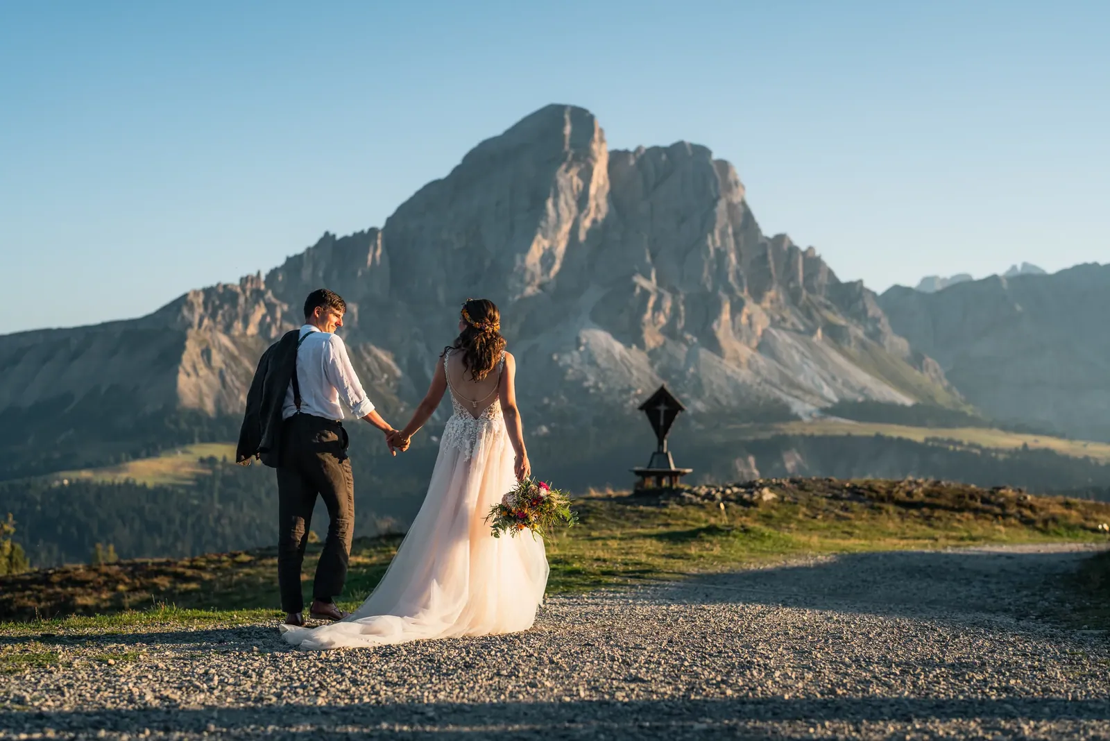 Brautpaar geht Hand in Hand zum Gipfelkreuz in den Dolomiten