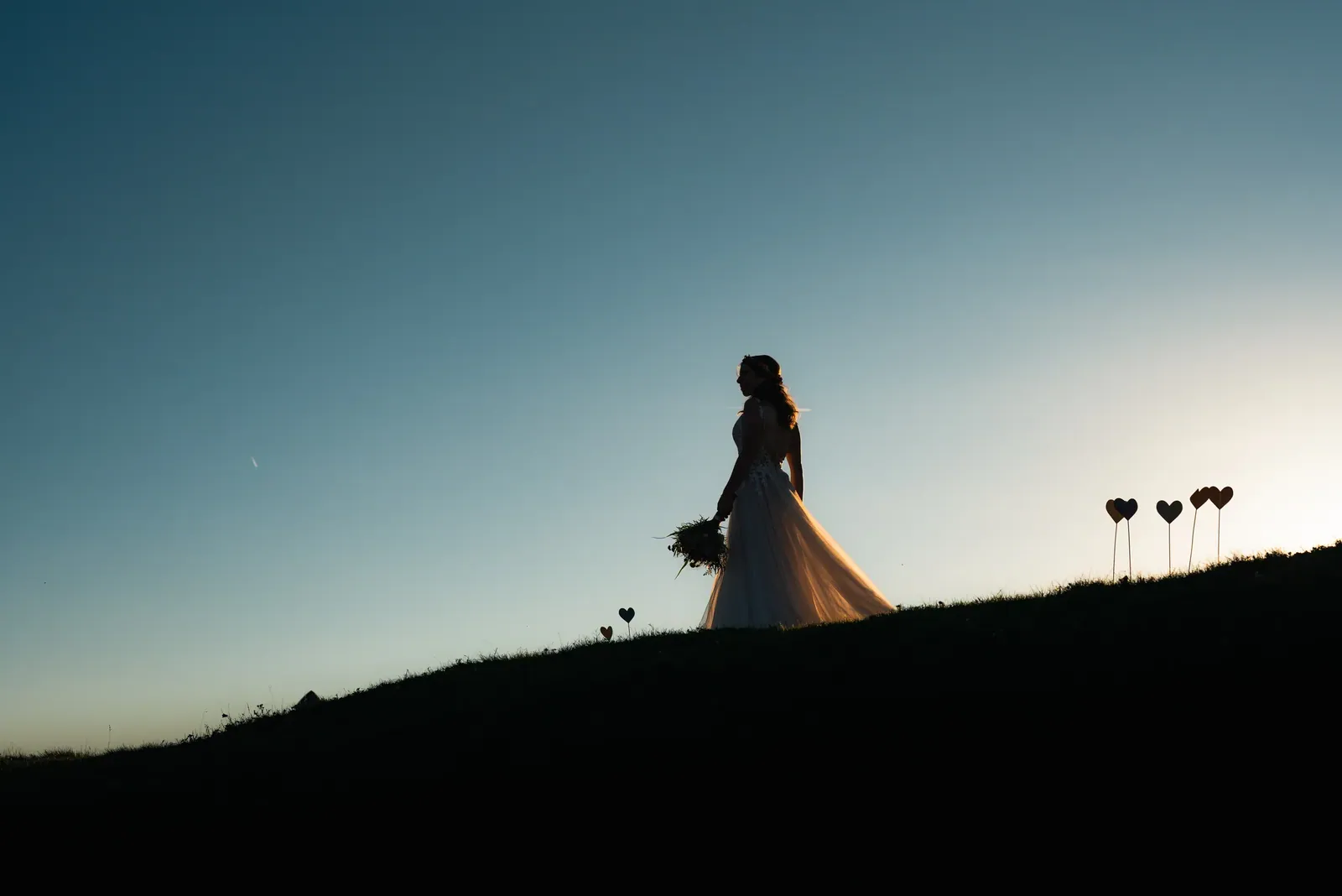Silhouette der Braut mit Herzen auf der Bergwiese bei Sonnenuntergang
