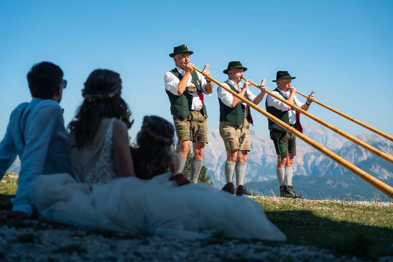 Brautpaar sitzt im Gras und hört den Alphornbläsern zu