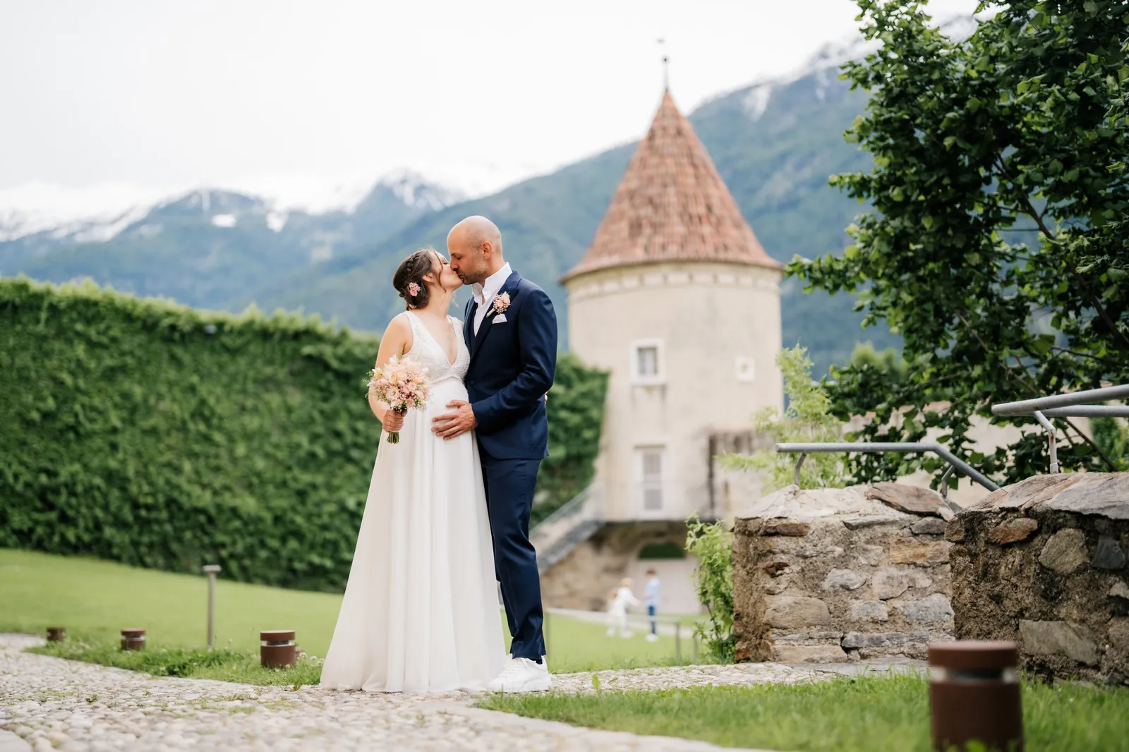 Brautpaar küsst sich vor dem Schlossturm, dahinter frisch verschneite Berge