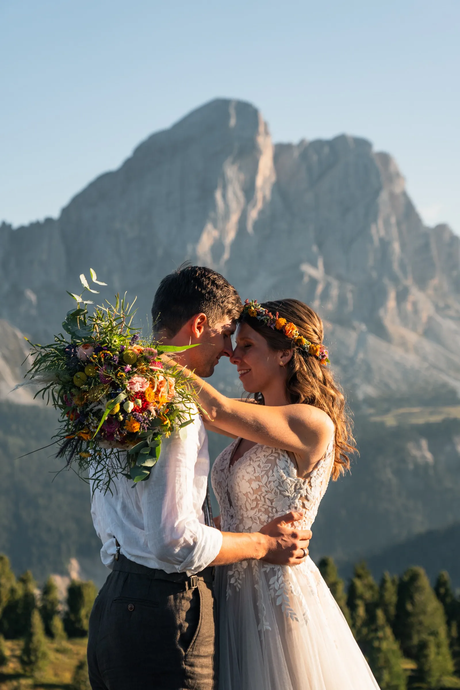 Brautpaar küsst sich mit Wildblumenstrauß in der goldenen Stunde vor dem Dolomitengipfel