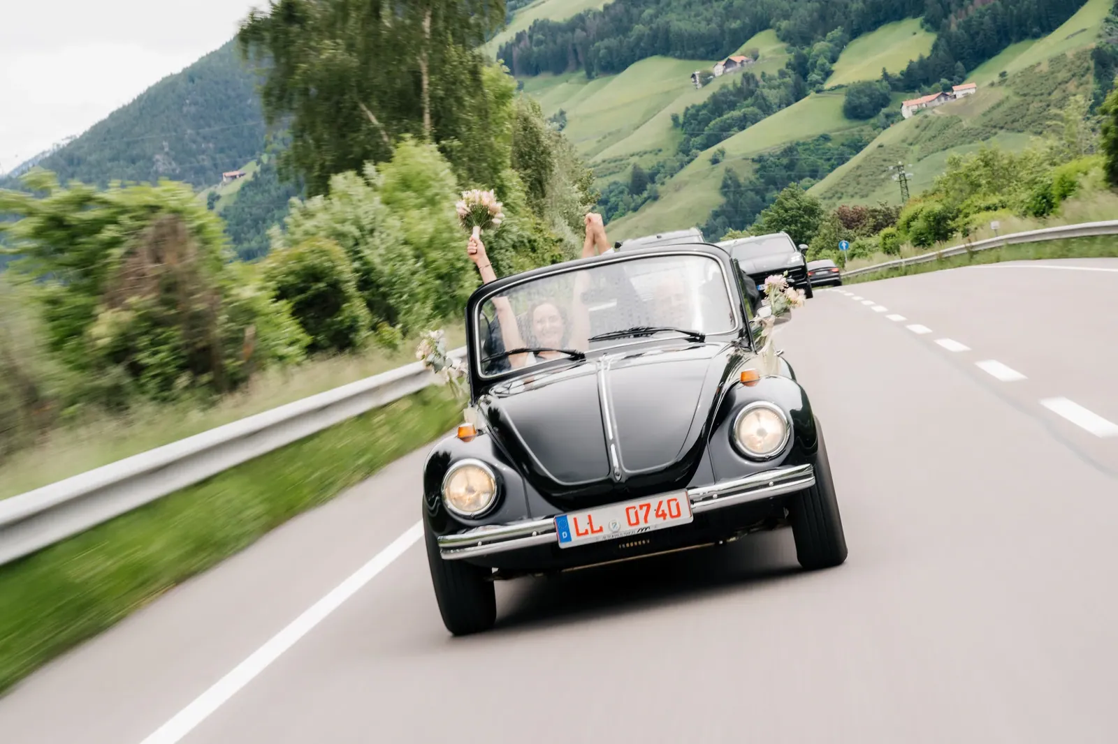 Brautpaar im schwarzen VW Käfer auf einer Bergstraße in Südtirol