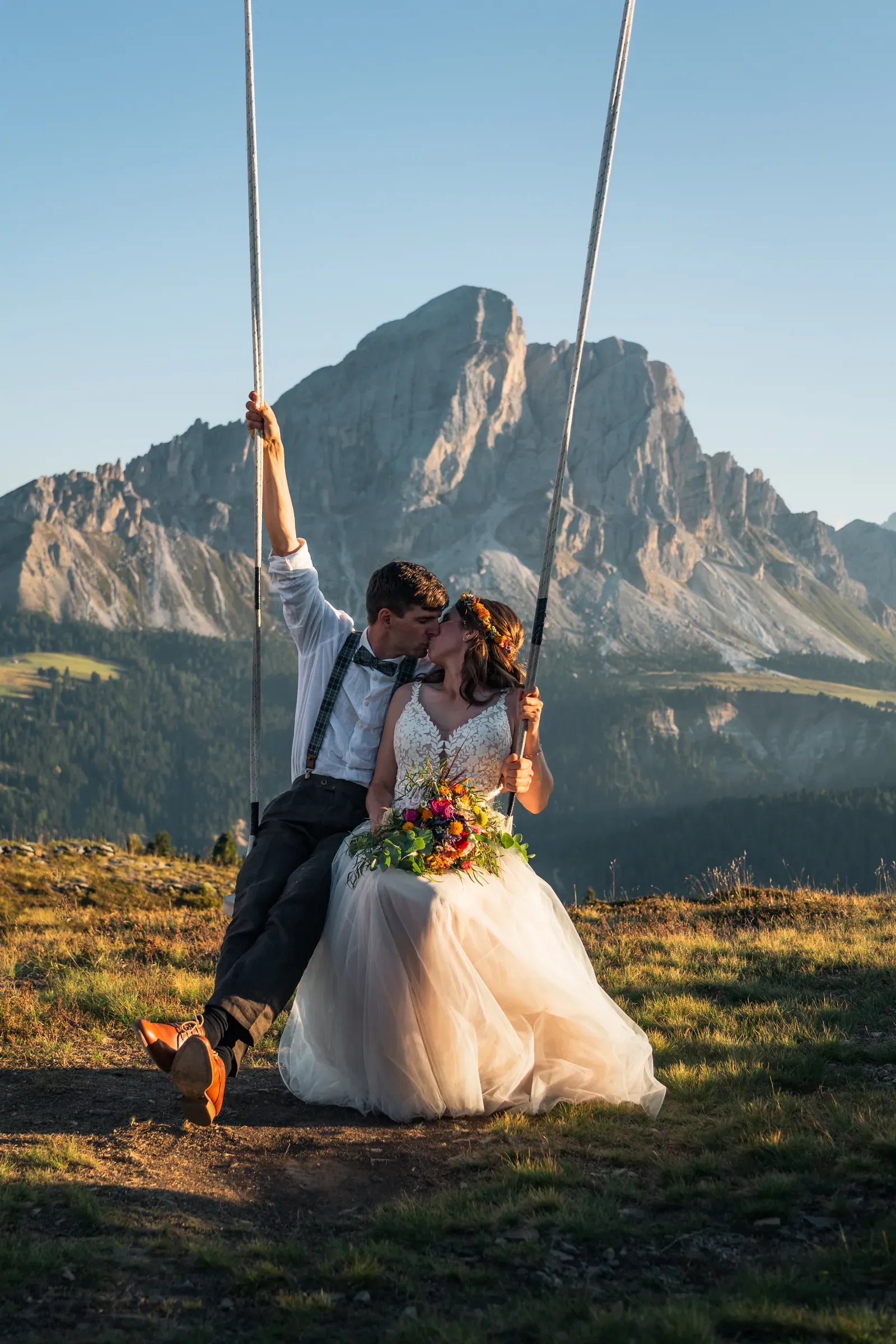 Brautpaar küsst sich auf einer Holzschaukel vor dem Dolomitengipfel