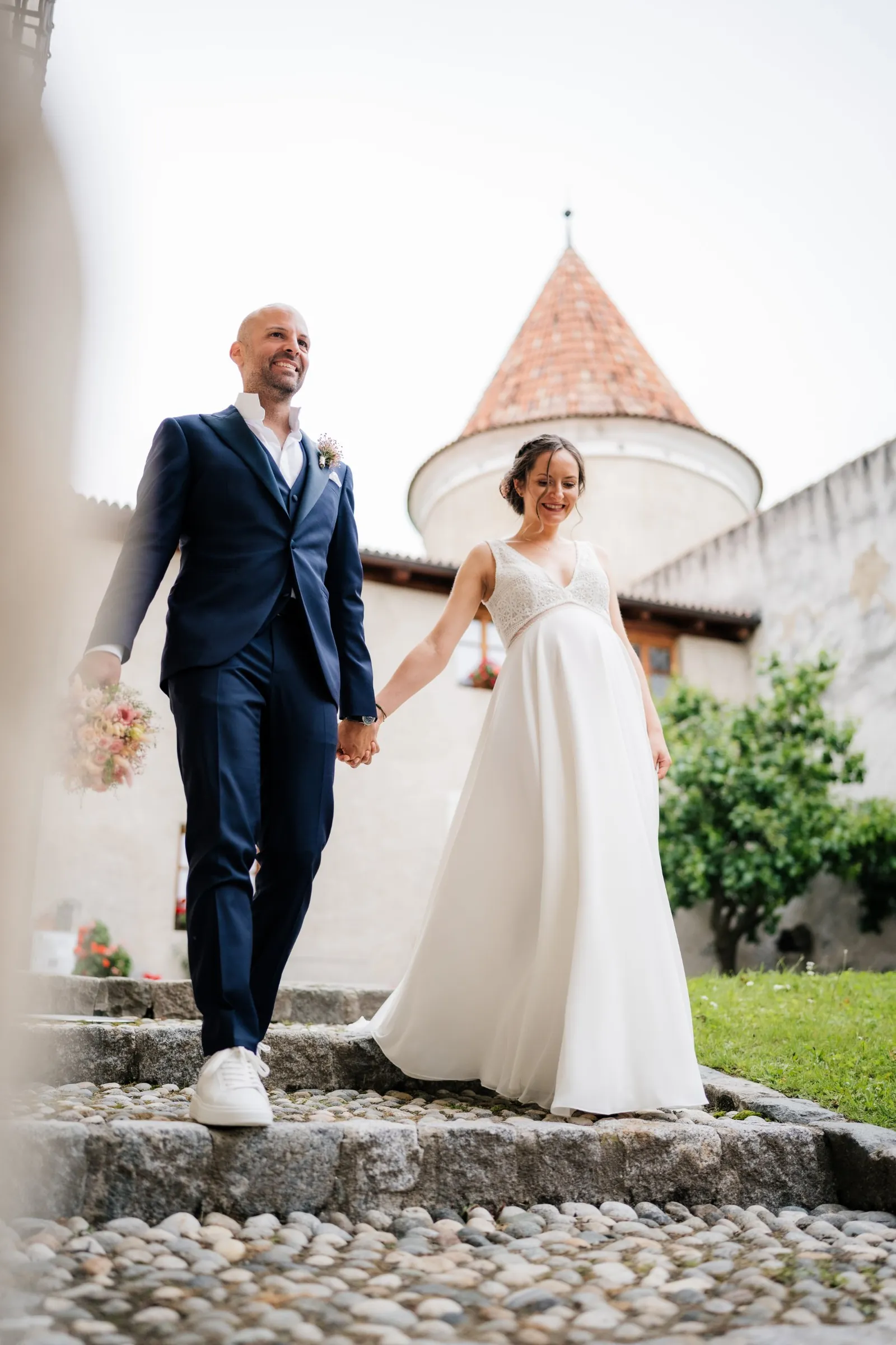Brautpaar geht lachend Hand in Hand die Steintreppe im Schloss hinunter