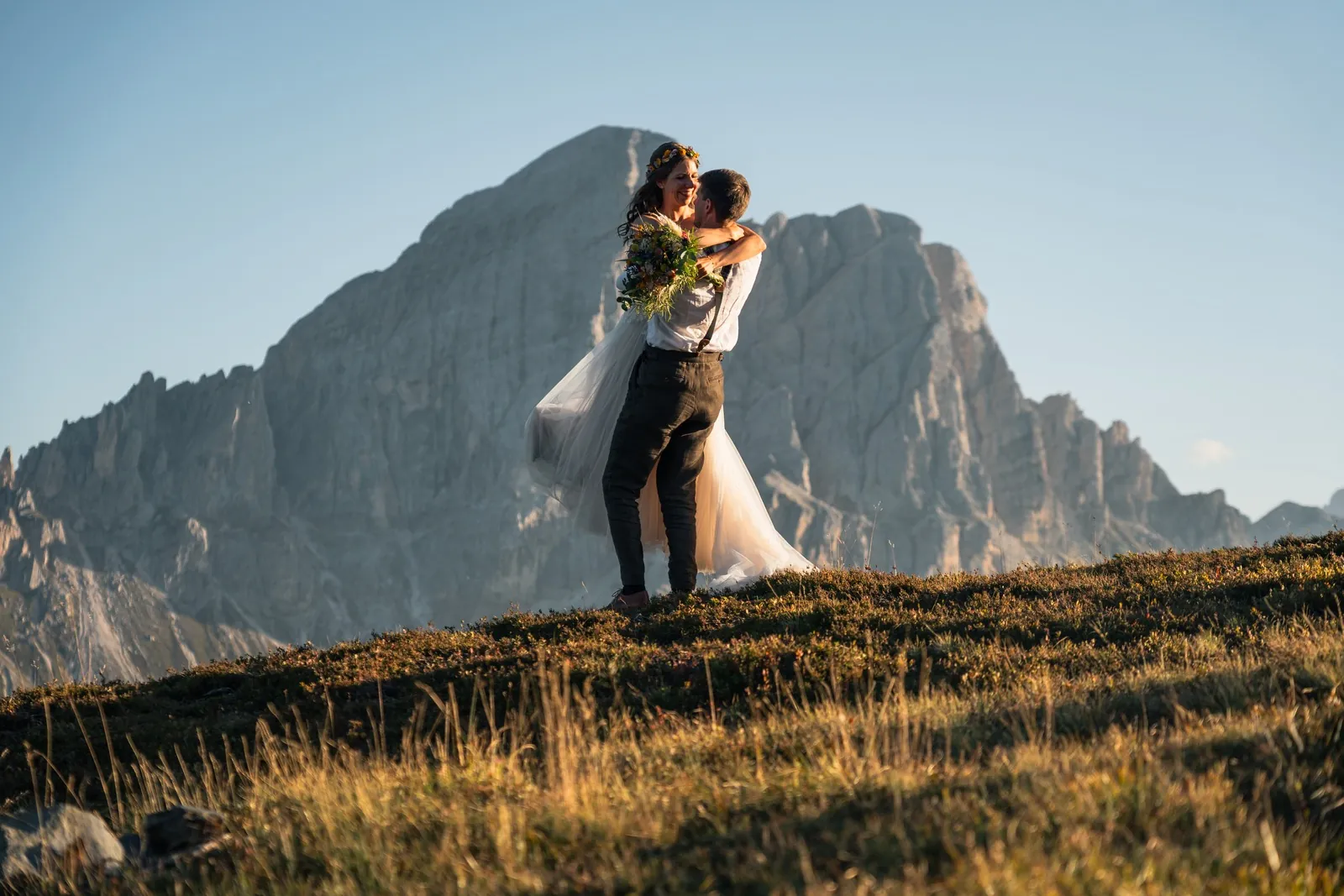 Bräutigam hebt die Braut vor der Dolomiten-Felswand im Abendlicht hoch