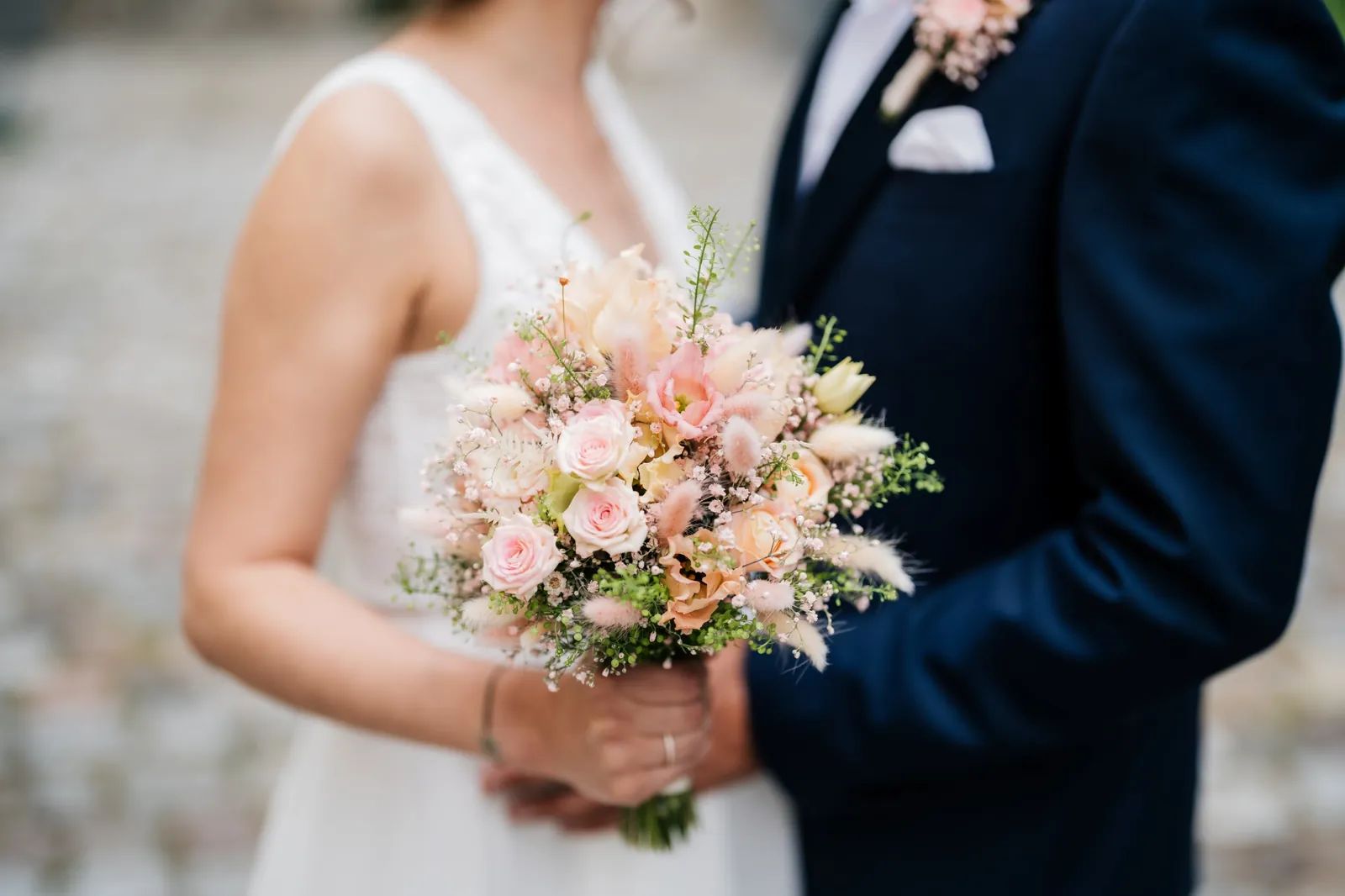 Brautstrauß in Pastelltönen zwischen Brautkleid und blauem Anzug