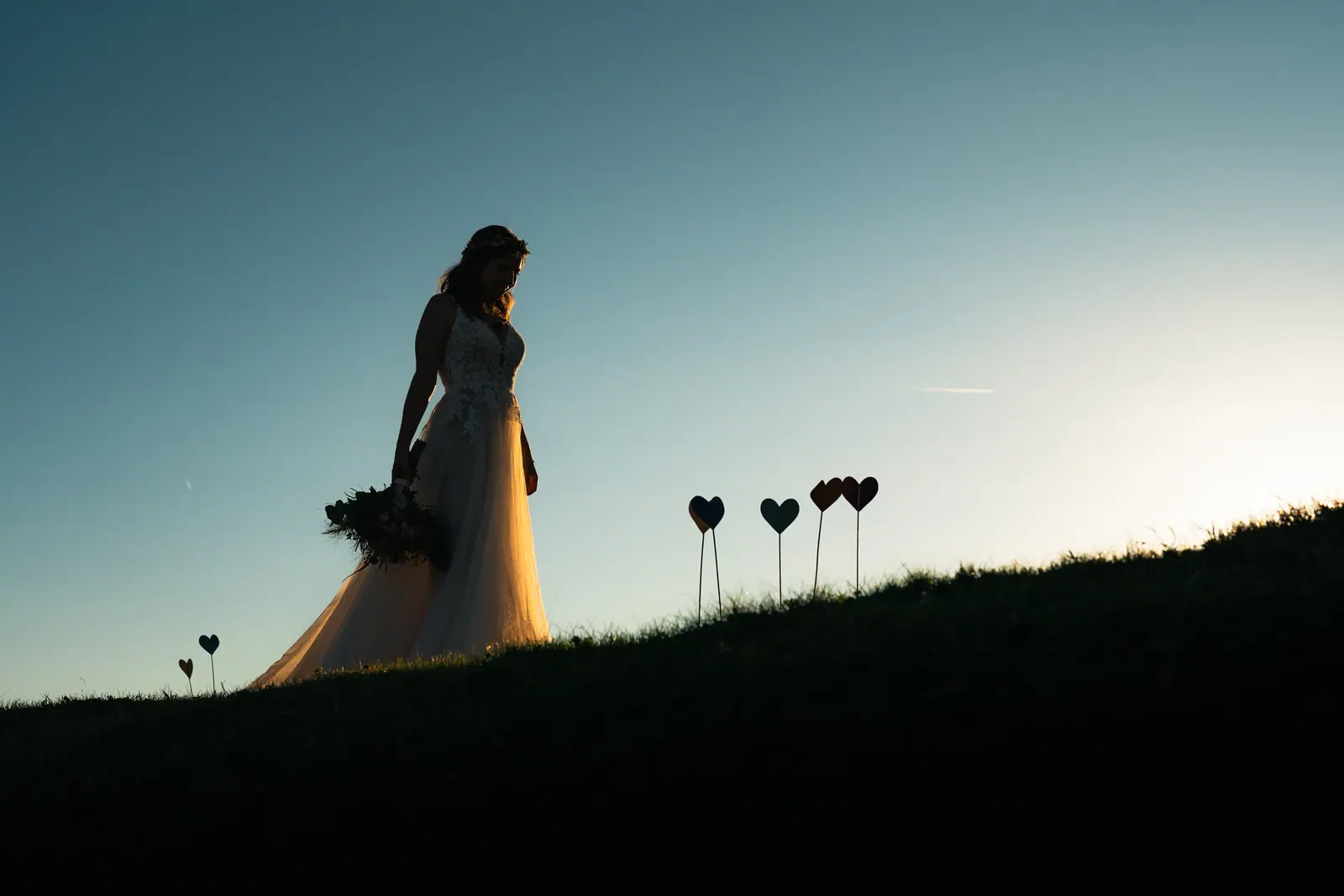 Silhouette der Braut mit Herzen auf der Bergwiese bei Sonnenuntergang