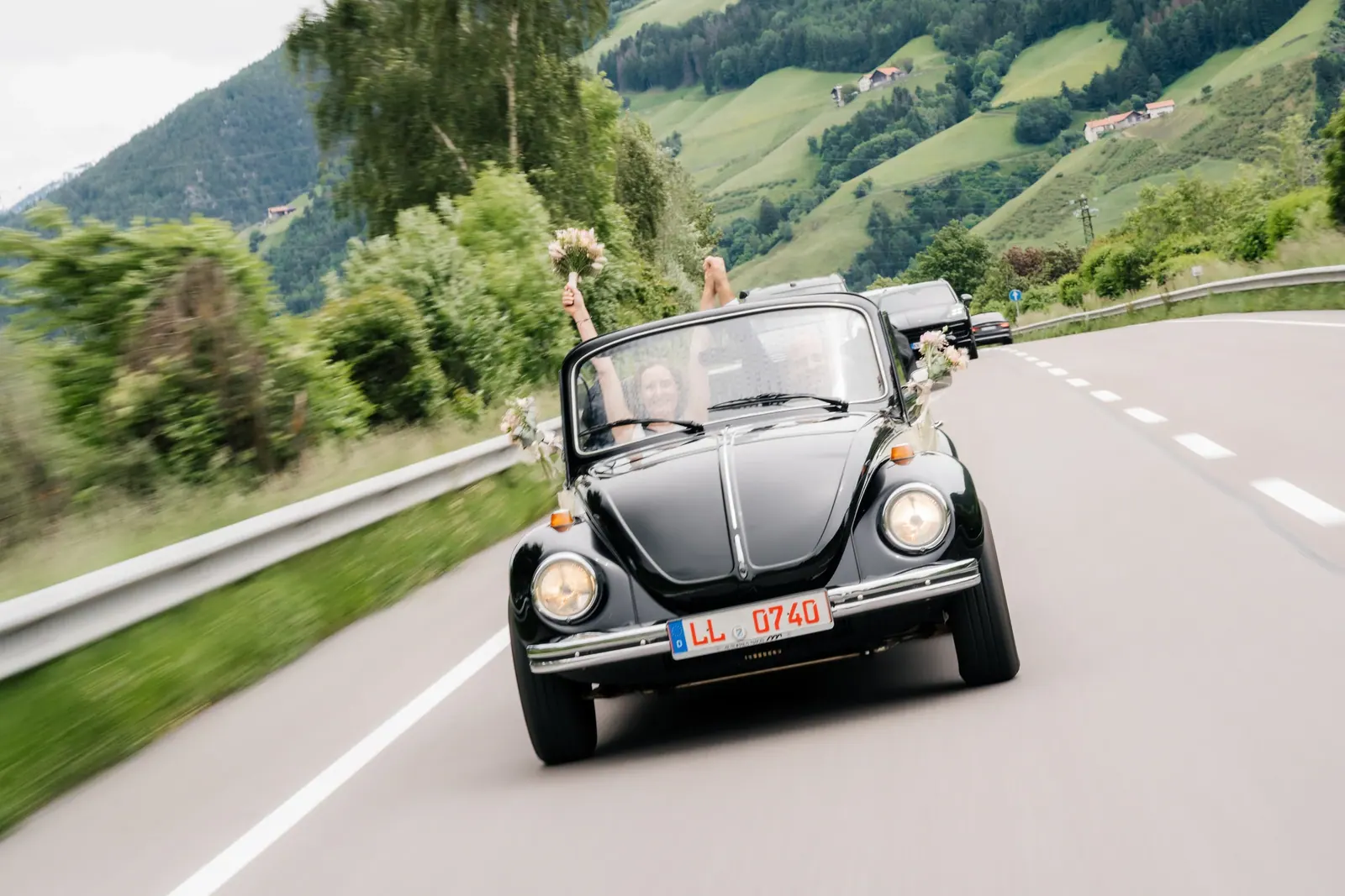 Brautpaar im schwarzen VW Käfer auf einer Bergstraße in Südtirol